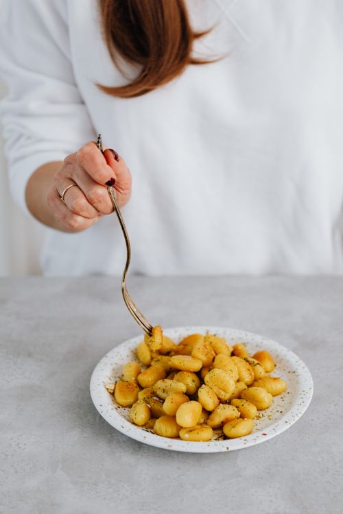 Free Person holding a fork with gnocchi on a ceramic plate in a minimalist setting. Stock Photo