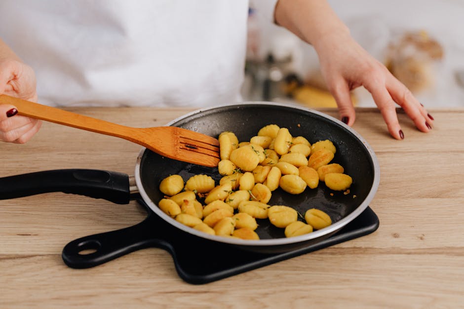 Close-up of cooking gnocchi in a pan using a wooden spatula on a wooden table.