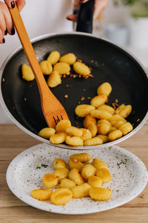 Free Gnocchi being transferred from pan to ceramic plate with wooden spatula. Stock Photo