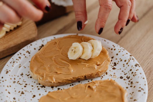 Hands prepare peanut butter banana toast on artistic ceramic plate for healthy breakfast.