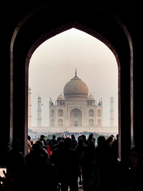 Free A crowd views the Taj Mahal through a distinctive archway, showcasing its architectural beauty. Stock Photo
