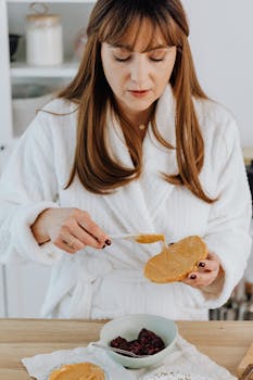 Woman in a robe spreading peanut butter on toast for a healthy snack.
