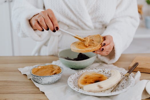 A person in a robe spreads creamy peanut butter on toast for breakfast.