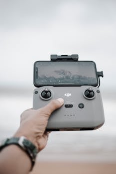 Close-up of a hand holding a drone controller with a smartphone displaying the camera view.
