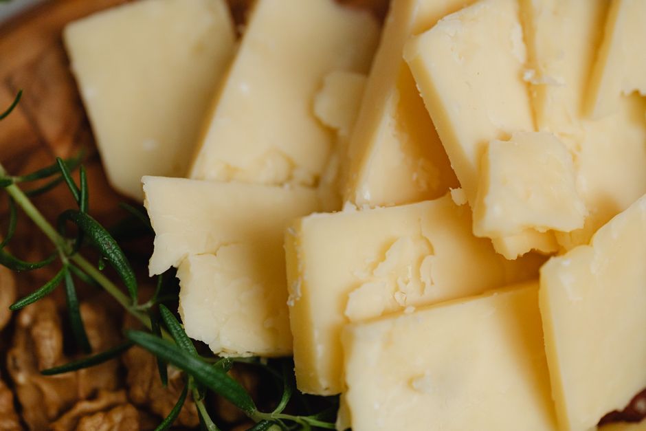 Pale yellow cheddar cheese cubes stacked on a wooden surface with herbs
