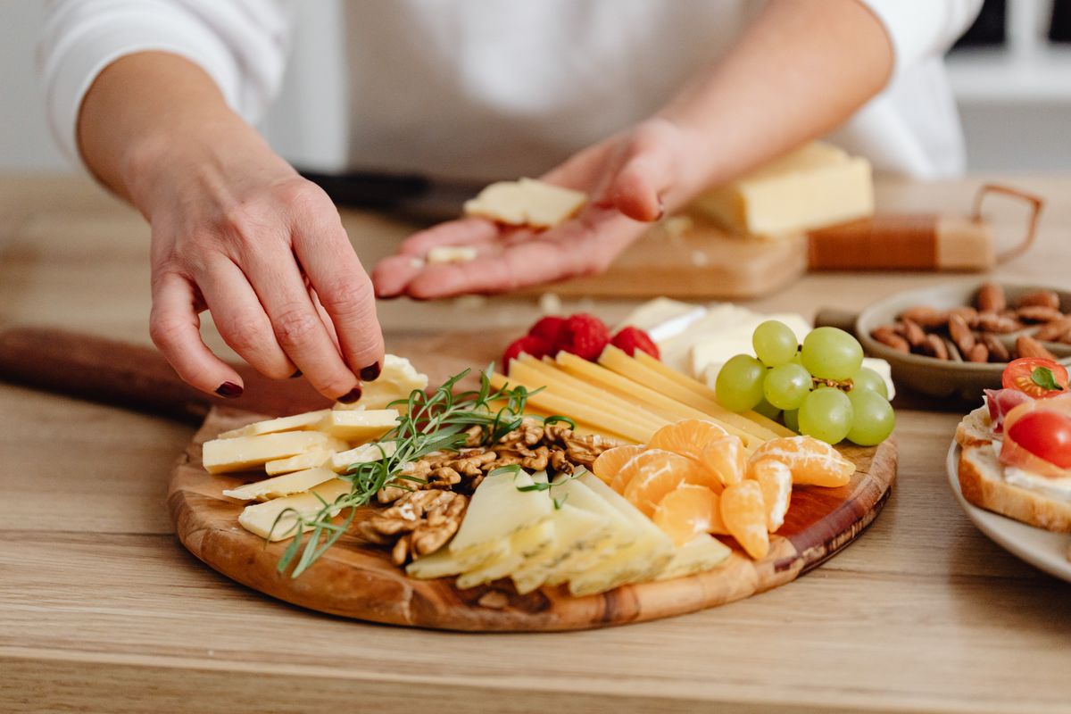 Mãos habilidosas de um produtor artesanal montando uma tábua de frios com queijos, embutidos e frutas para demonstração premium.