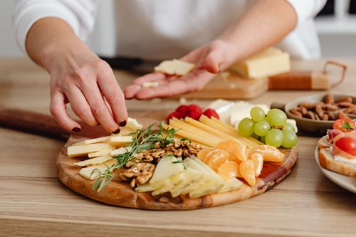 Free Close-up of hands crafting a gourmet cheese, fruit, and nut charcuterie board. Stock Photo