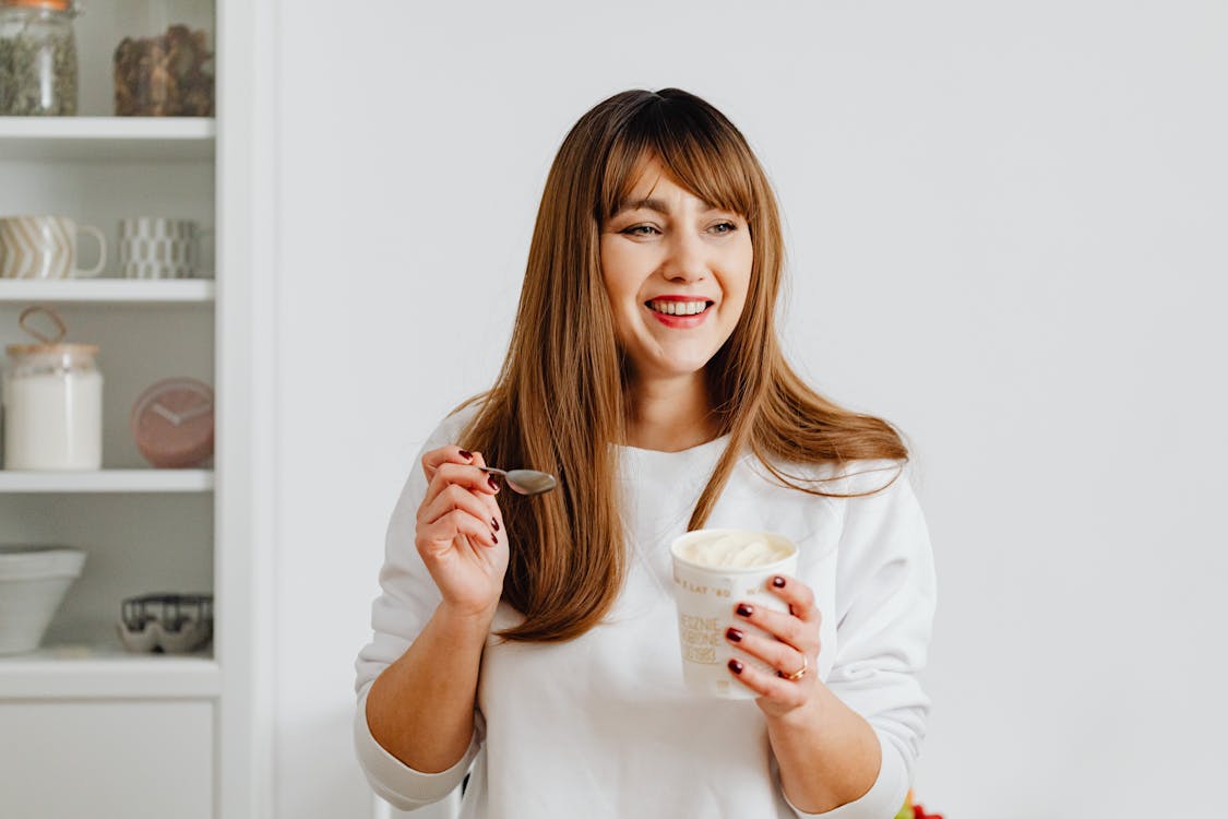 Woman with Brown Hair Holding a White Cup with Ice Cream while Smiling