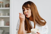 Brunette woman savoring a tasty ice cream indoors with eyes closed.