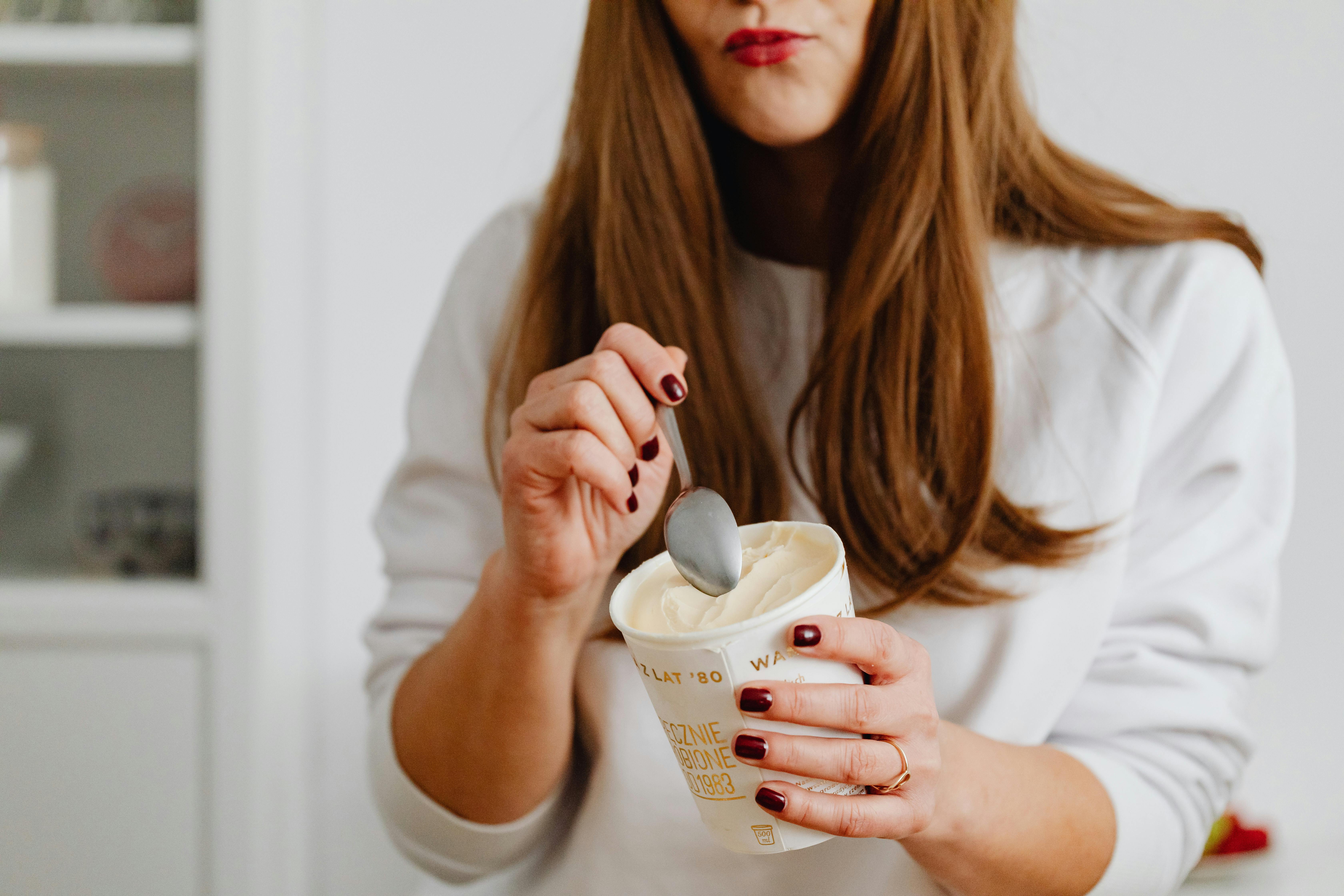 A woman with red nail polish enjoying a cup of ice cream indoors, using a spoon.