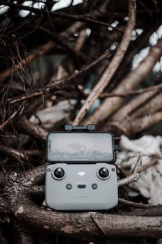 Close-up of a drone controller and smartphone resting on tree branches, highlighting outdoor technology.