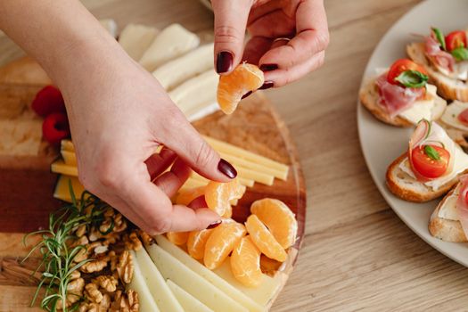 A close-up of hands preparing a delicious charcuterie board with cheese, citrus, and rustic baguette slices.