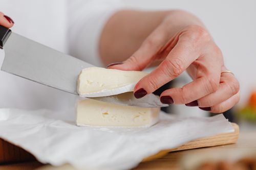 Free A hand with manicured nails slices creamy cheese on a wooden board. Stock Photo