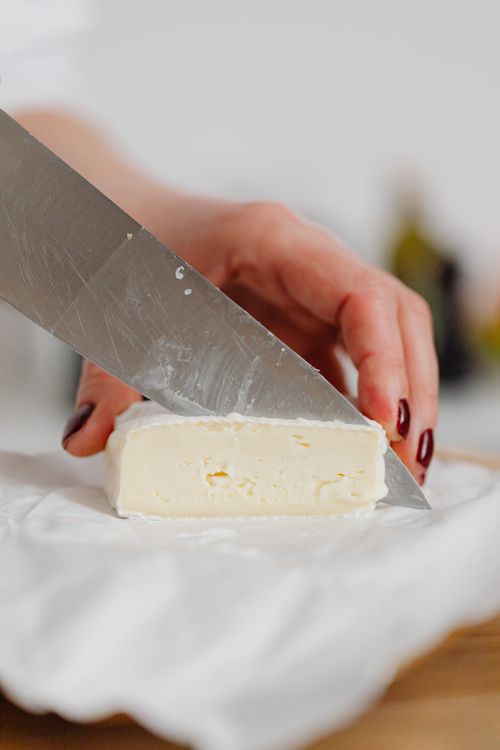Free A person slicing creamy brie cheese with a knife, showcasing texture and freshness. Stock Photo