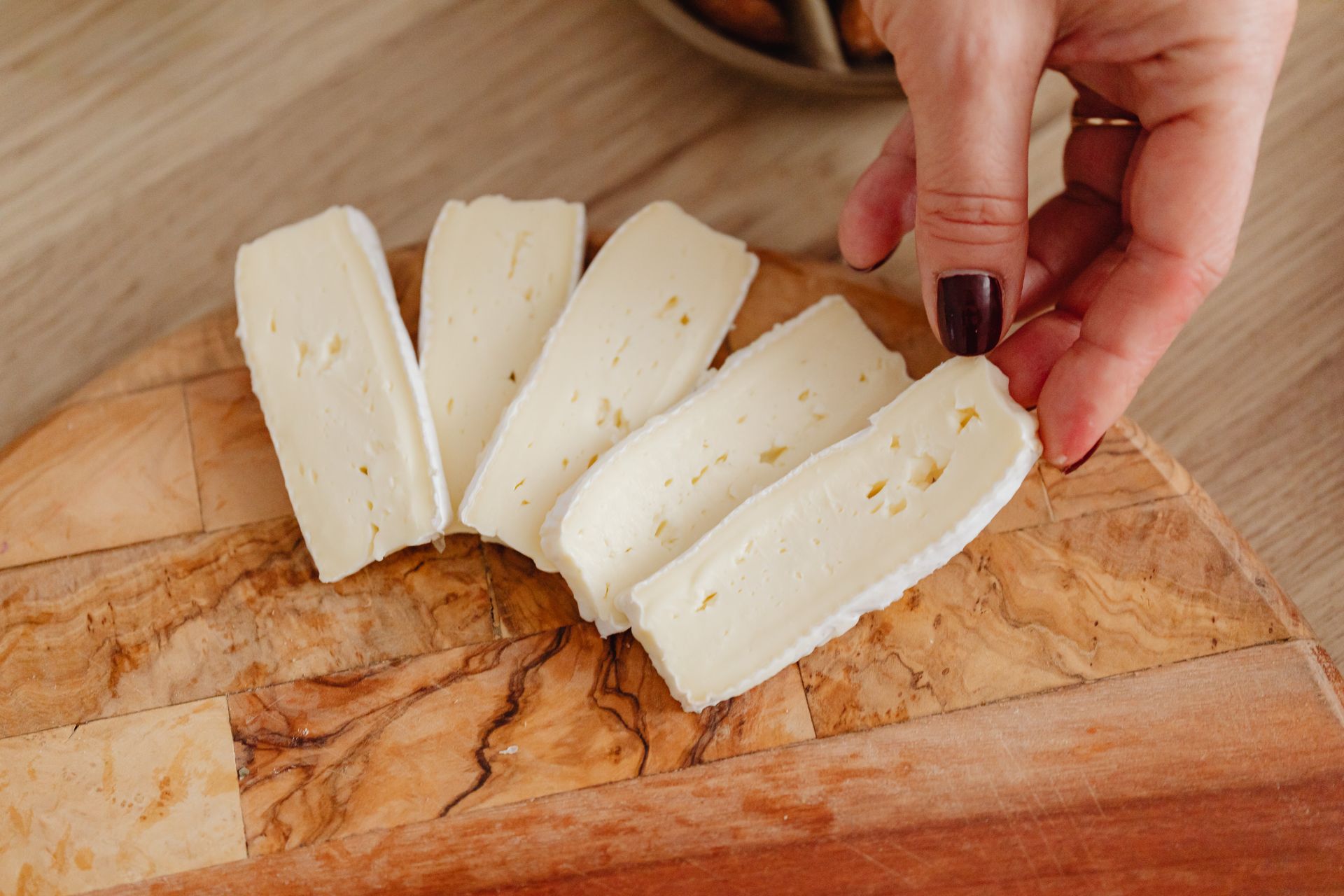 Hand holding fresh creamy brie cheese slices on wooden board, perfect for gourmet dishes.