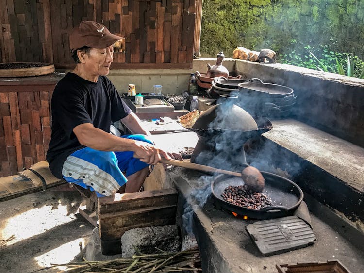 A Man In Black Shirt Sitting While Roasting Coffee On A Pan