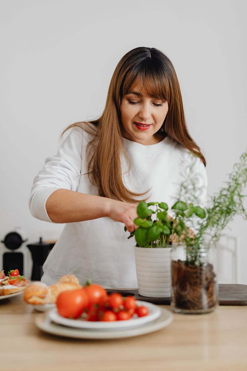 Woman in white shirt caring for herbs and tomatoes in kitchen setting. Fresh and vibrant.