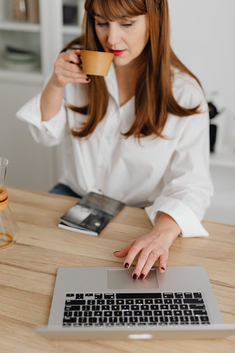A Woman Drinking Coffee While Using A Laptop