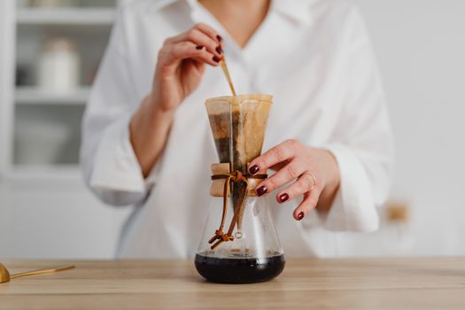 Close-up of a woman preparing drip coffee with a Chemex in a modern kitchen.