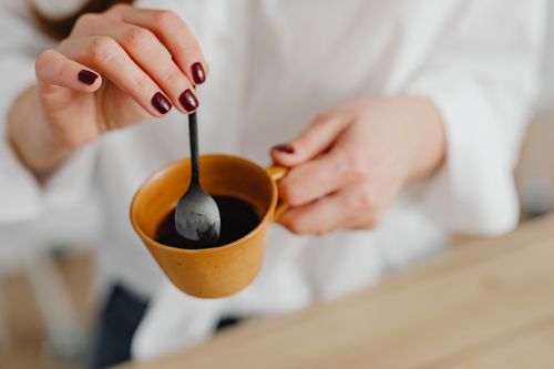 Free Close-up of a woman stirring coffee in a ceramic mug, showcasing manicured nails. Stock Photo