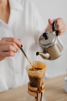 Close-up of hands brewing coffee with a stainless steel kettle and filter.
