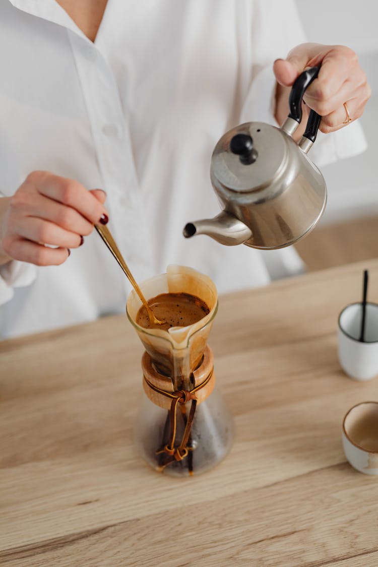 Person Pouring Water From A Kettle Into A Jar