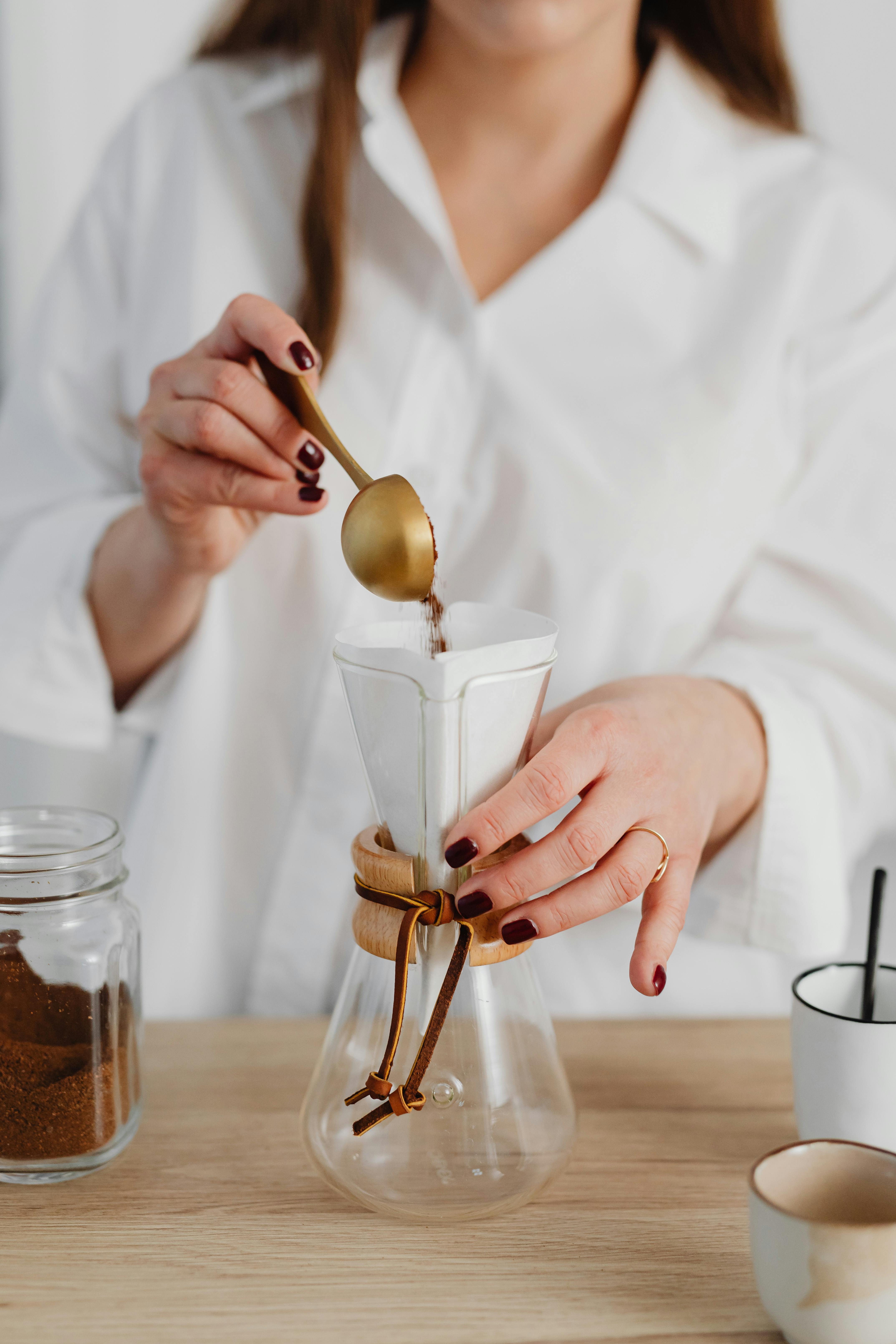 a woman in white long sleeves holding a golden spoon and glass jar