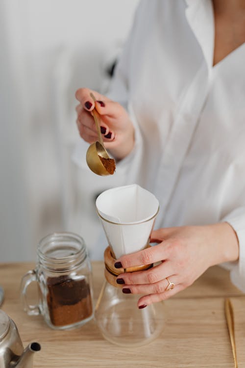 Person Scooping Brown Powder Into a Jar With White Filter