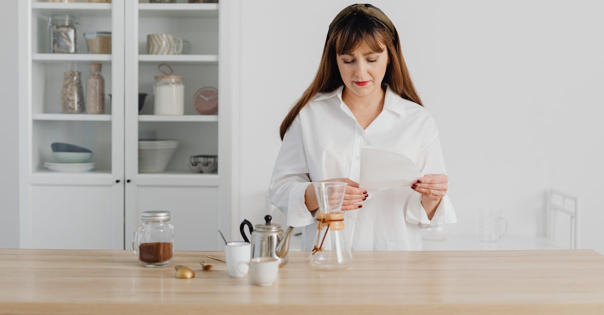 A woman reading instructions while making coffee in a bright, modern kitchen setting.