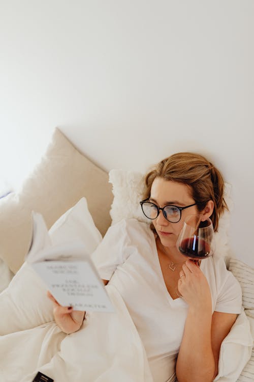 Woman Drinking Wine and Reading Book in Bed