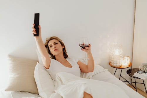 Free A Woman Holding a Glass Wine and a Remote Control Stock Photo