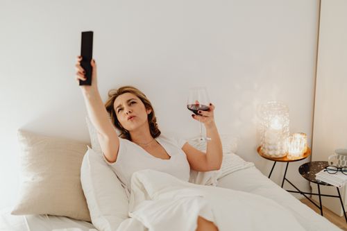 Free Woman relaxing in bed with wine, remote in hand, surrounded by candles. Stock Photo