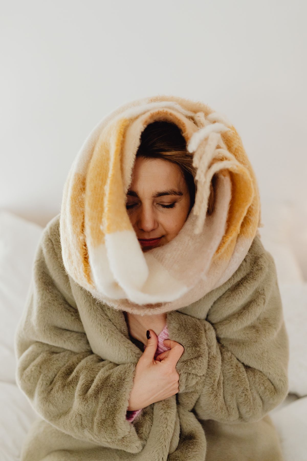 Woman indoors wrapped in a thick fleece blanket pulled up around her head and shoulders to keep warm