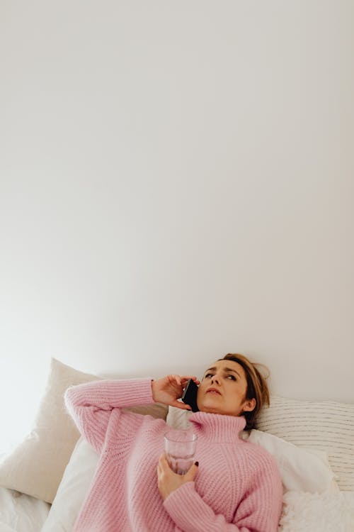 Free A Woman Lying on the Bed with Sweater Using a Phone Stock Photo