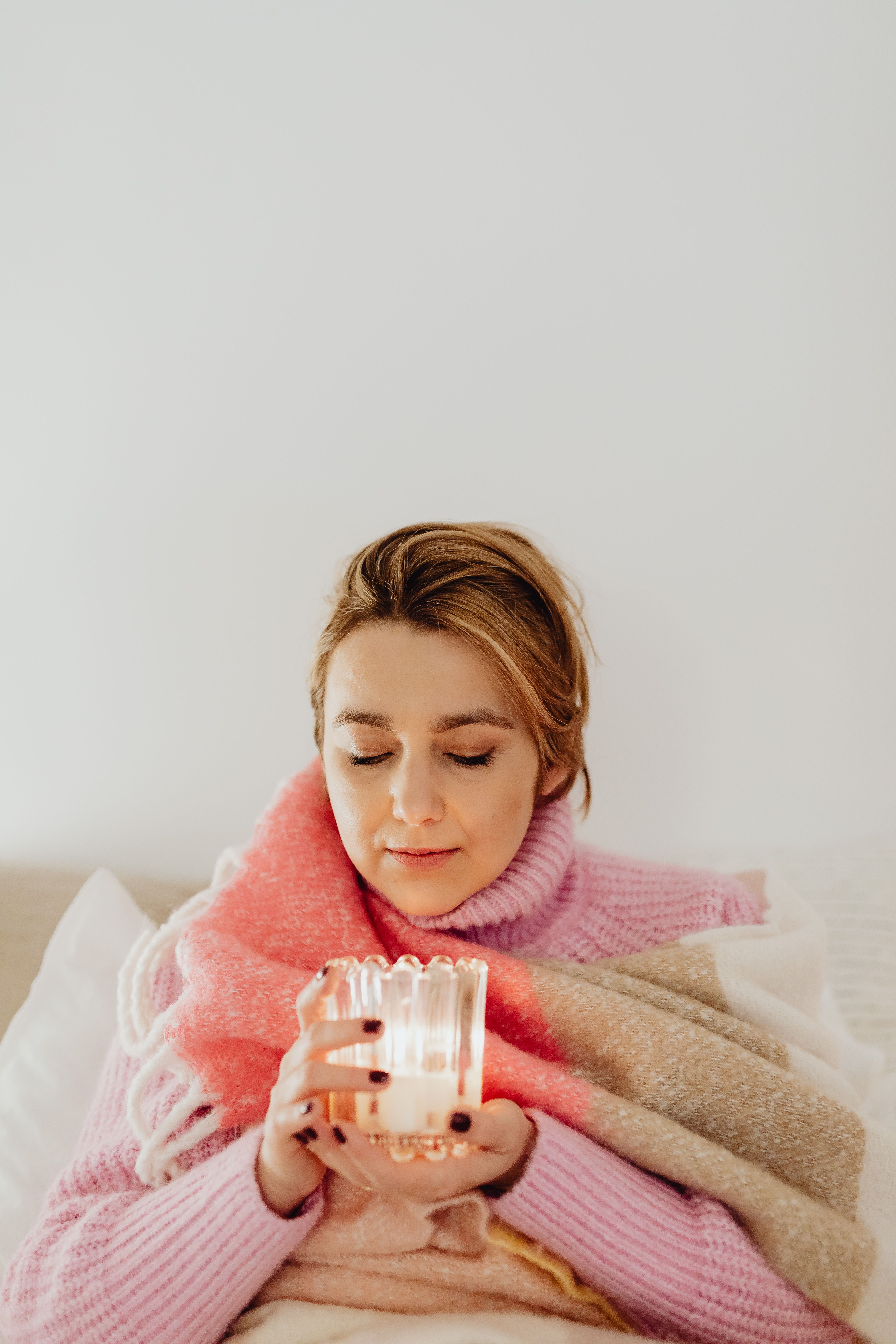 Woman wrapped in a soft blanket, holding a candle, enjoying a peaceful indoor moment.