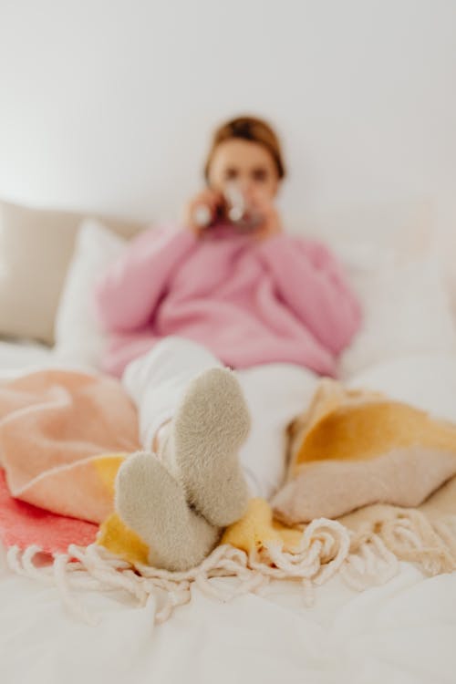 Free Woman Wearing Pink Long Sleeves and Beige Socks Sitting on Bed Stock Photo