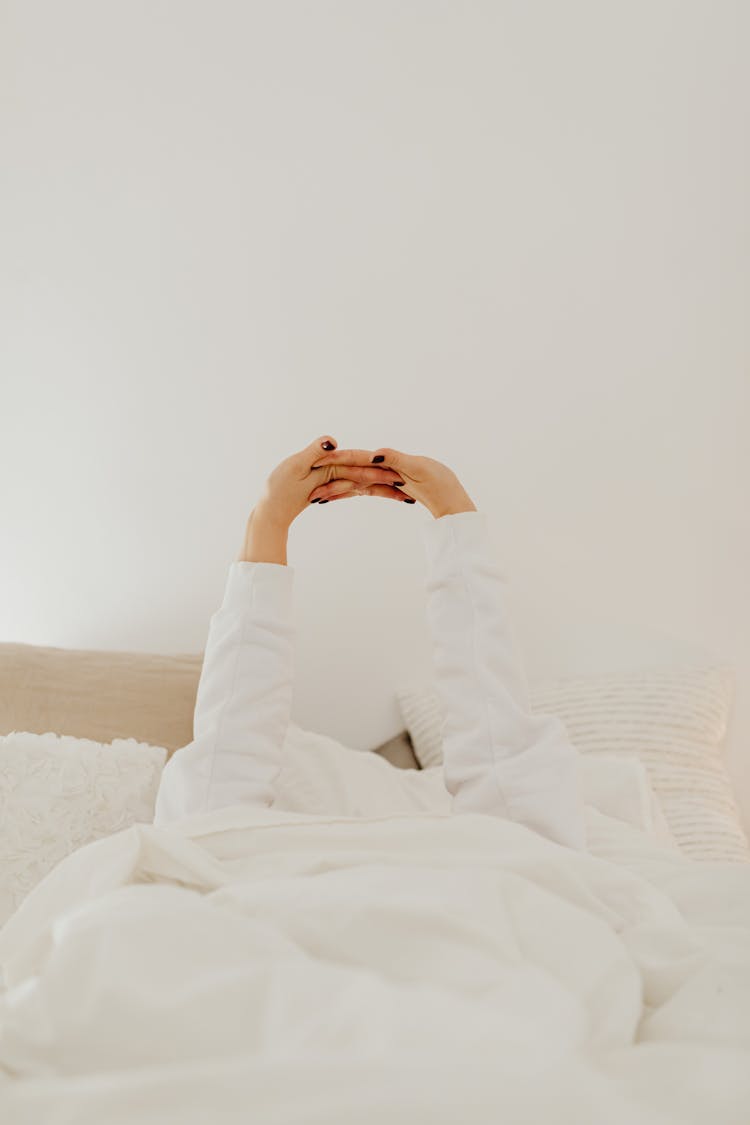 Person Stretching Arms And Hands Lying On Bed