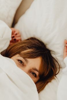 Woman relaxing in bed, wrapped in a soft white blanket, exuding warmth and comfort.