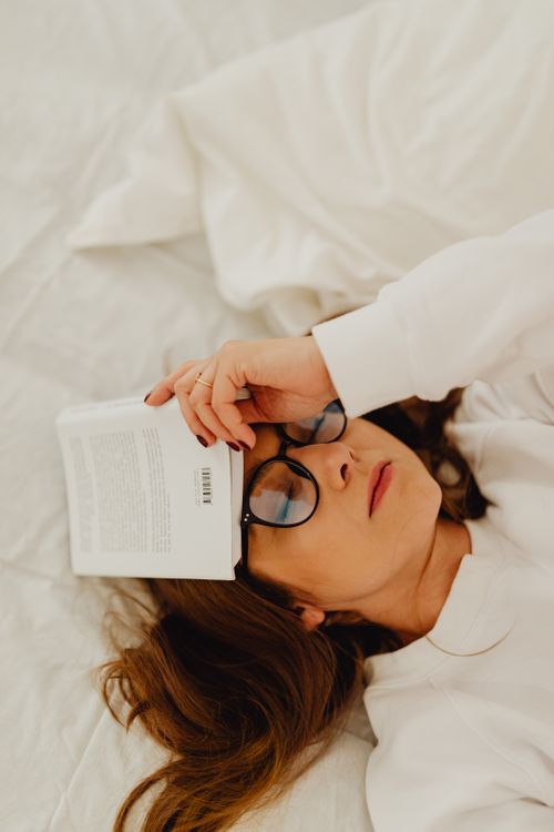 Free A woman in white lies with a book on her head, appearing relaxed and contemplative. Stock Photo