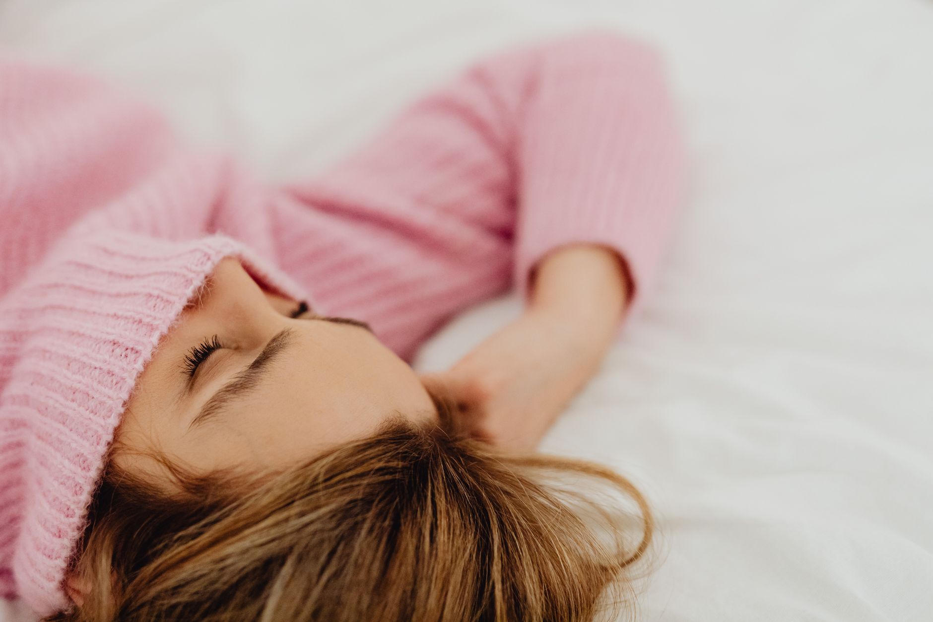 A serene image of a woman sleeping peacefully in a cozy pink sweater on a white bed.