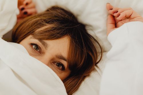 Free Cozy close-up of a woman with manicured nails peeking out from a white sheet. Stock Photo