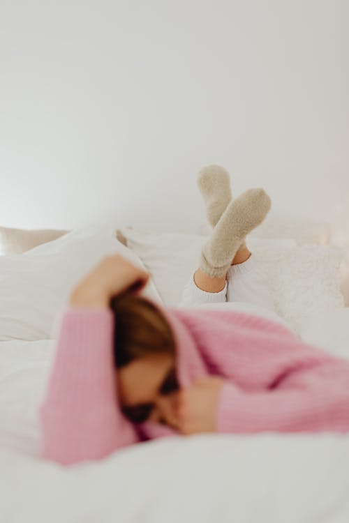 Free Woman in Pink Sweater Wearing Socks on Bed Stock Photo