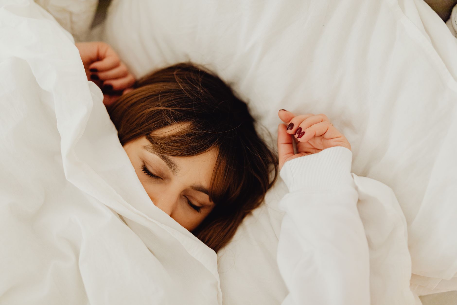 失眠解決方法全攻略:從習慣養成到環境調整 A woman peacefully sleeping under a white blanket in a cozy bed setting.