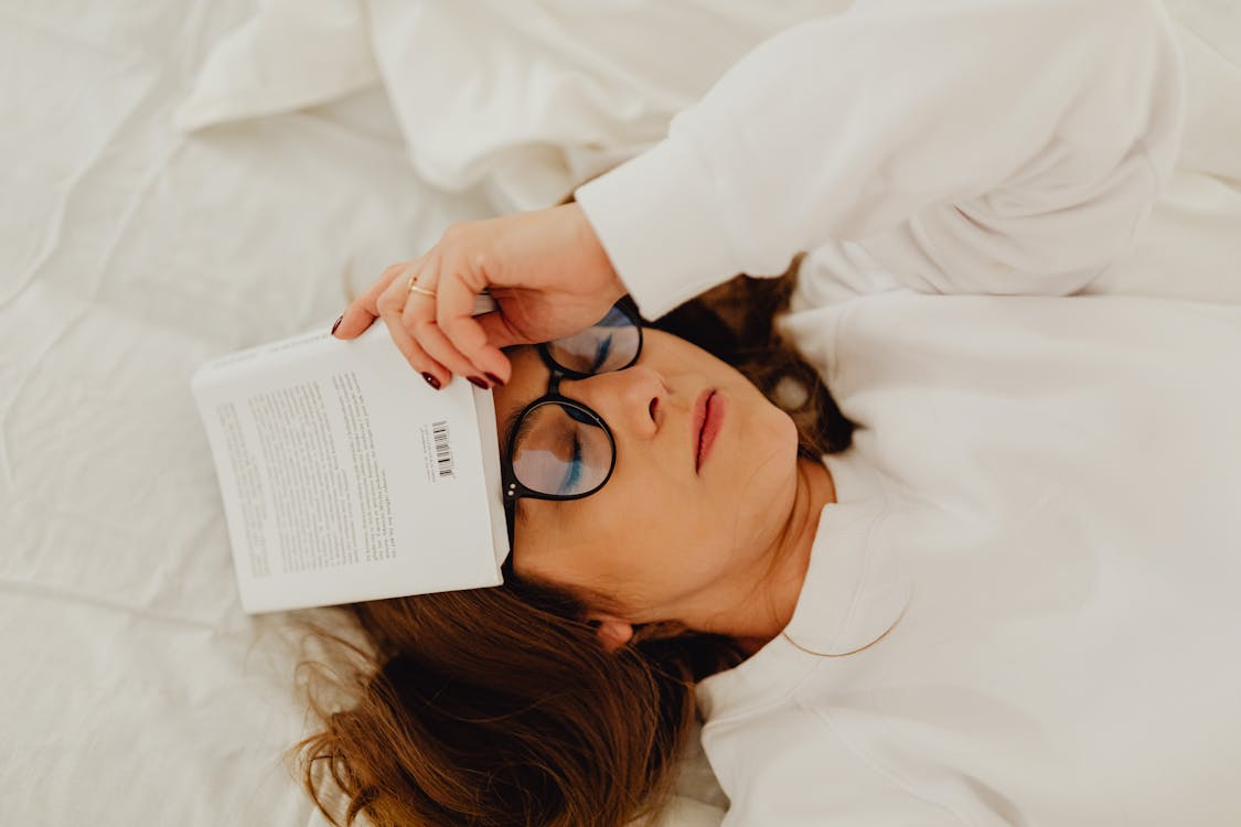 Free A Woman Wearing Jacket and Eyeglasses Holding a Book While Lying Down Stock Photo
