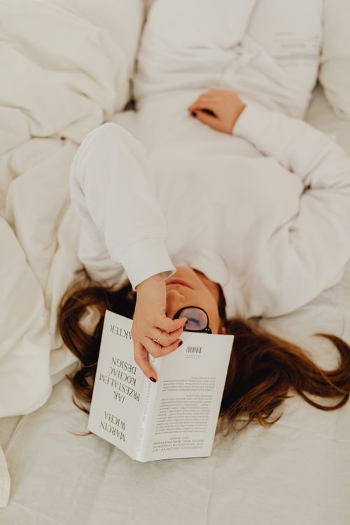 Free Woman lying down on bed reading a book, relaxing with closed eyes. Stock Photo