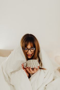 Woman wrapped in a blanket enjoying a warm beverage, creating a cozy and relaxing atmosphere.