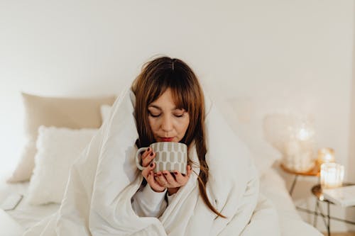 Free Woman Wrapped in White Blanket Holding a Ceramic Mug Stock Photo