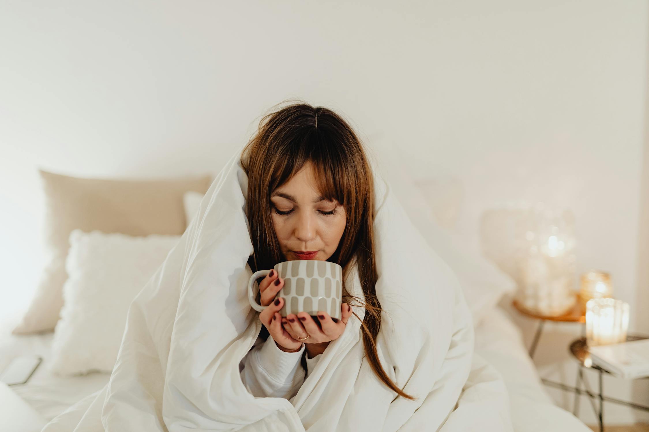 Image of woman wrapped in white blanket holding a ceramic mug