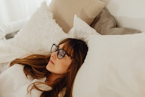 Free A Woman Lying on the Pillow Wearing Eyeglasses Stock Photo