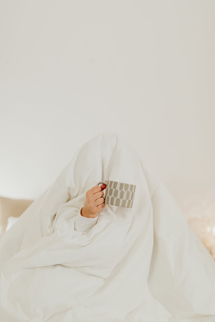 Person Hiding Under A White Blanket Holding A Ceramic Mug